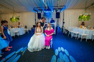 Wedding reception with attendees on blue carpet under stage lighting and white tent ceiling.