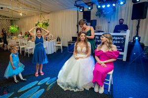 Wedding reception scene with guests in blue and pink dresses dancing on a blue-carpeted floor under stage lighting.