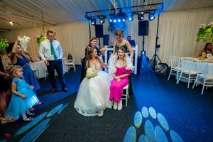 Wedding reception dance floor scene with blue lighting and white chairs in a tent venue.