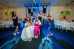 Festive wedding reception with guests dancing under blue spotlights and decorative lighting.