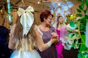 Wedding reception guests dancing and celebrating in a decorated venue with string lights and green accents.