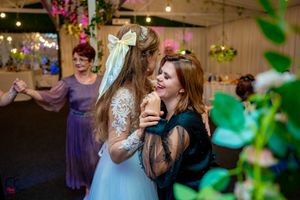 Lively wedding reception dance floor with guests celebrating under decorative lighting and greenery.