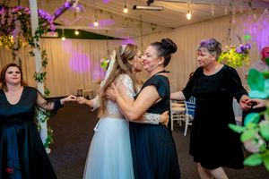 Wedding guests dancing and celebrating in a decorated indoor venue with purple accent lighting.