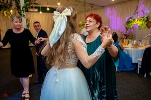 Wedding party dancing and having fun at reception with purple uplighting and overhead string lights.