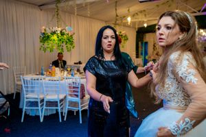 Wedding celebration with guests dancing in an indoor venue decorated with hanging greenery and string lights.