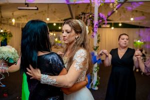 Wedding reception guests dancing and celebrating on the dance floor under purple lighting and string lights.