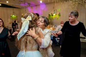 Heartfelt embrace during wedding celebration with guests and decorative lighting.