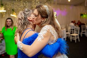 Wedding reception embrace with guest in royal blue dress under ambient lighting.