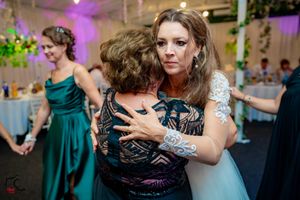 Emotional embrace during wedding reception under purple ambient lighting and floral decorations.