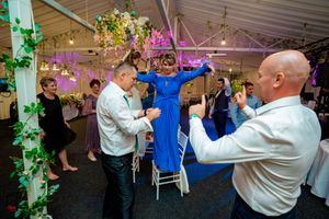 Wedding party dancing under decorative lighting and floral arrangements in reception tent.