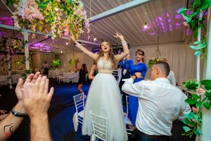 Indoor wedding celebration showing guests dancing under decorative lighting and green vine accents.