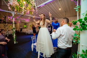 Wedding reception venue with floral decor and guests dancing under colorful party lights.