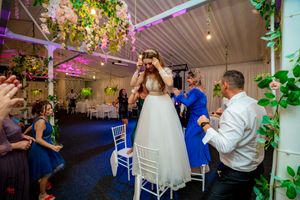 Wedding venue with elegant ceiling decorations and guests dancing under purple and green lighting.