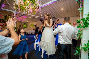 Wedding celebration in a decorated indoor space with guests dancing under ambient lighting.