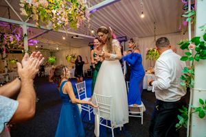 Wedding party dancing in a decorated indoor venue with blue carpeting and floral accents.