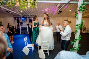 Wedding reception venue decorated with green vines and pink lighting showing guests dancing and celebrating.