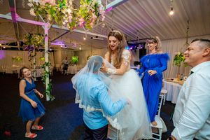 Lively dance floor at wedding reception with decorative lighting and hanging floral arrangements.