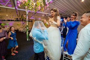 Festive wedding reception with guests dancing beneath floral decorations and purple accent lighting.