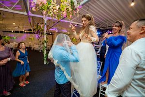 Wedding guests dancing and celebrating under hanging greenery and string lights at indoor venue.