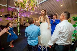 Wedding party dancing and celebrating in an elegant venue with string lights and greenery.