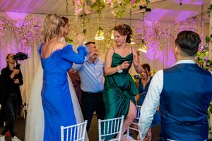 Wedding celebration with guests dancing under hanging floral arrangements and purple mood lighting.