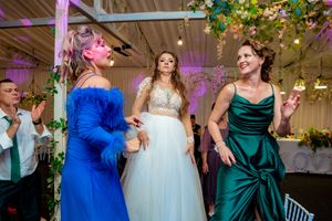 Wedding reception guests dancing and celebrating in a decorated venue with purple lighting and floral decor.