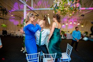 Wedding party members dancing and celebrating under purple lighting and floral ceiling decorations.