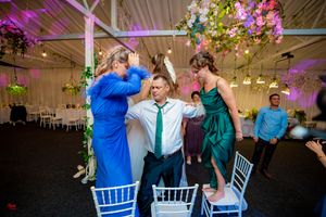 Wedding reception venue featuring elegant white chairs, purple lighting and suspended floral arrangements.