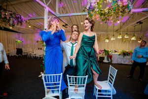 Wedding party dancing and celebrating in a reception venue decorated with purple lighting and floral arrangements.