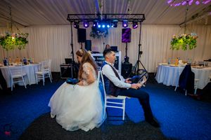 Wedding reception venue with blue carpeting and white drapes features elegant lighting and table settings.