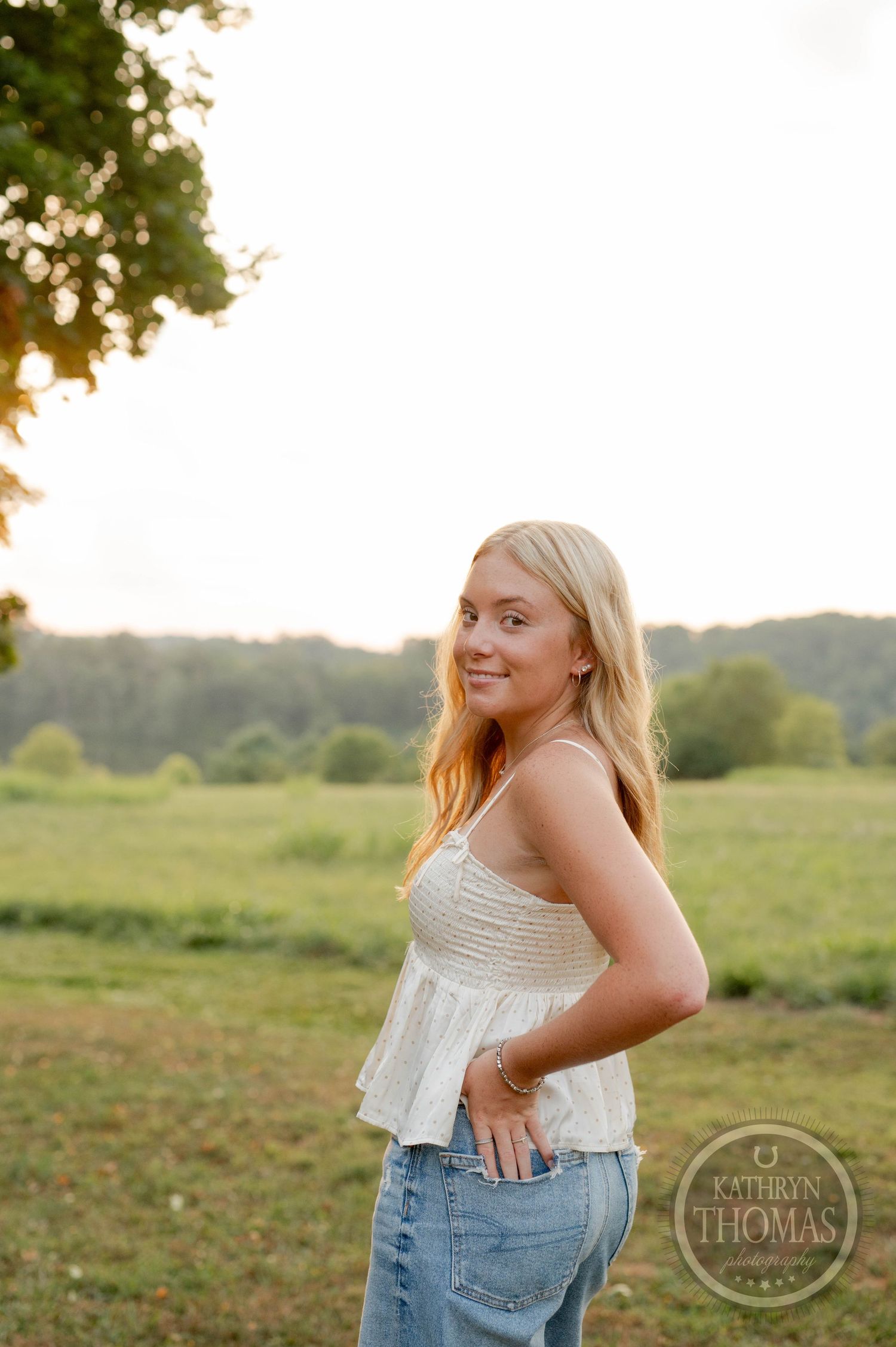 Sunset portrait against trees wearing white summer top and casual denim.