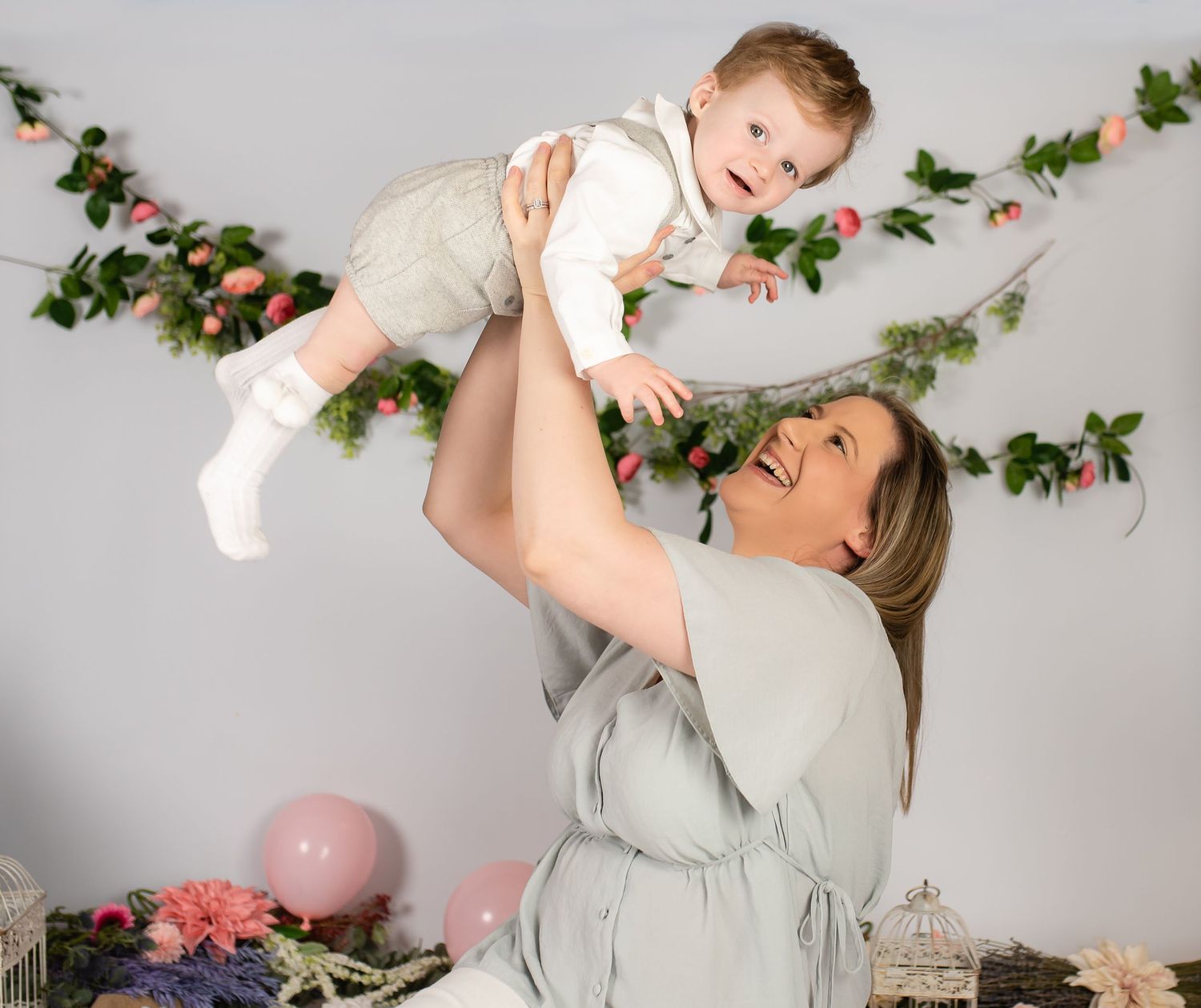 A joyful moment captured against a gray wall decorated with floral vines and a pink balloon in a lifestyle photoshoot setting.