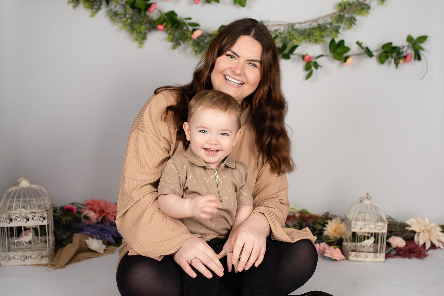 A parent and child wearing matching tan sweaters sit together for a holiday photo with decorative garland and lanterns.