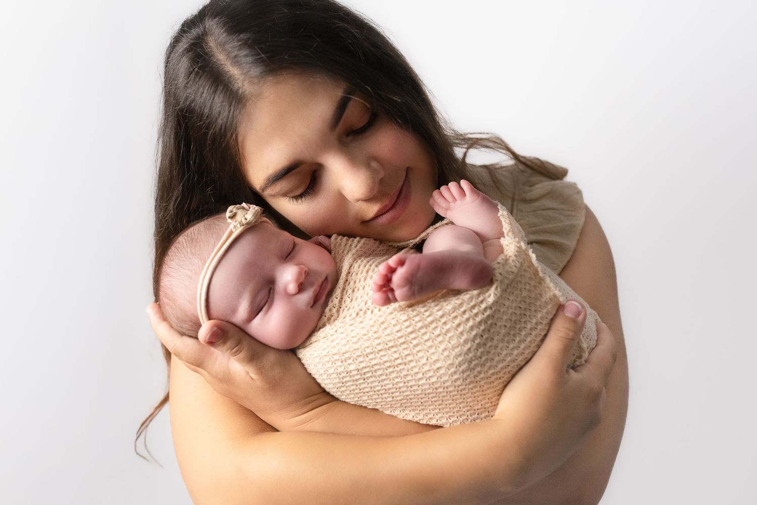 A tender moment showing sleeping newborn twins wrapped in a knitted blanket being held against a white background.