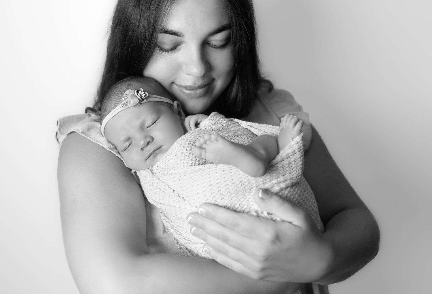 A tender black and white portrait of a peaceful sleeping newborn baby being cradled in soft fabric.