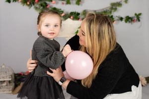 A parent and child pose together with a pink balloon during a holiday photo session against a decorated background.