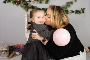 A tender holiday portrait with a pink balloon against a backdrop of festive garland decorations and props.