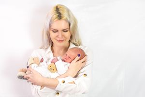 A peaceful portrait of a newborn baby being cradled in white against a bright studio background.