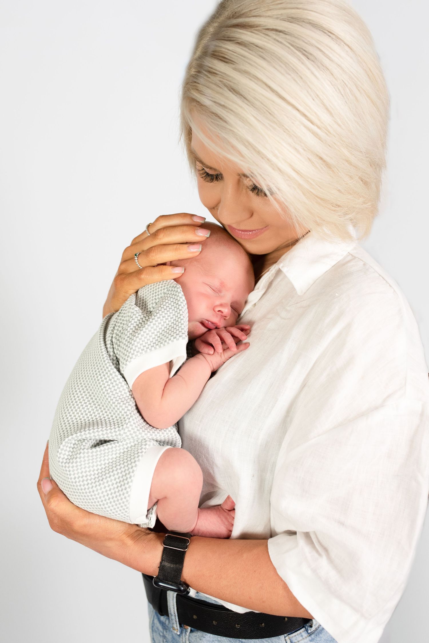 A parent in a white shirt tenderly holds and comforts a sleeping newborn baby wearing a dotted onesie.