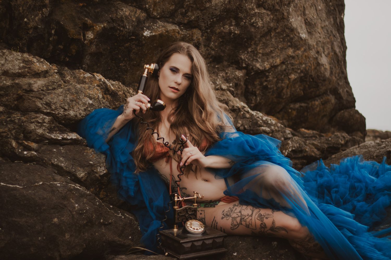 Ethereal portrait of a woman in flowing blue fabric posed dramatically against rocky backdrop.