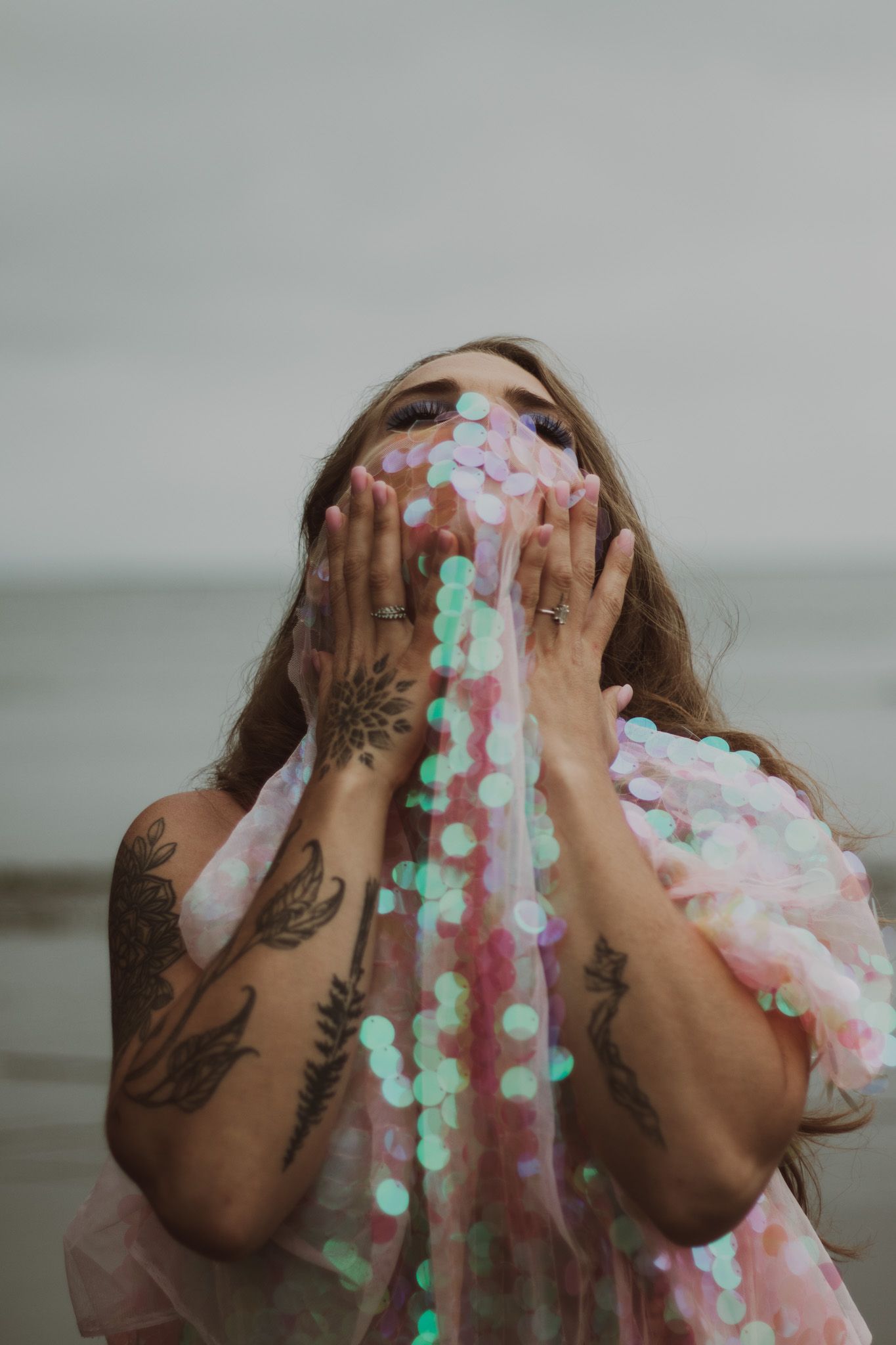 Artistic portrait with sparkly iridescent fabric and tattoo covered arms.