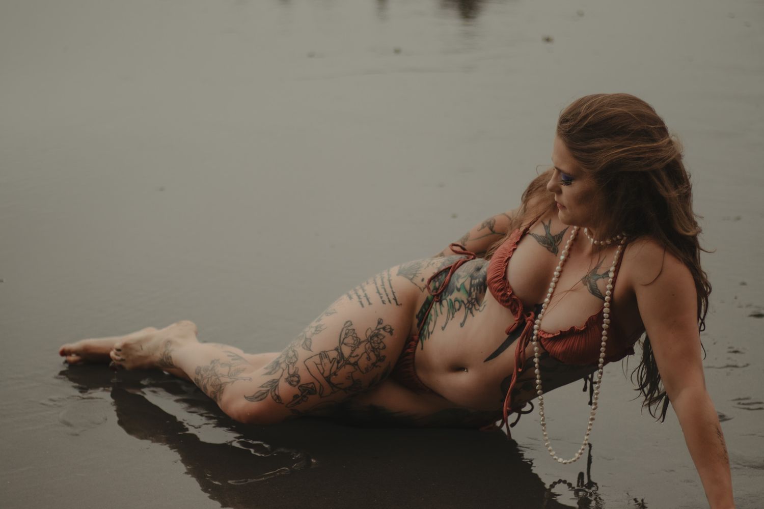 Moody beach portrait showing tattooed figure laying in shallow water.