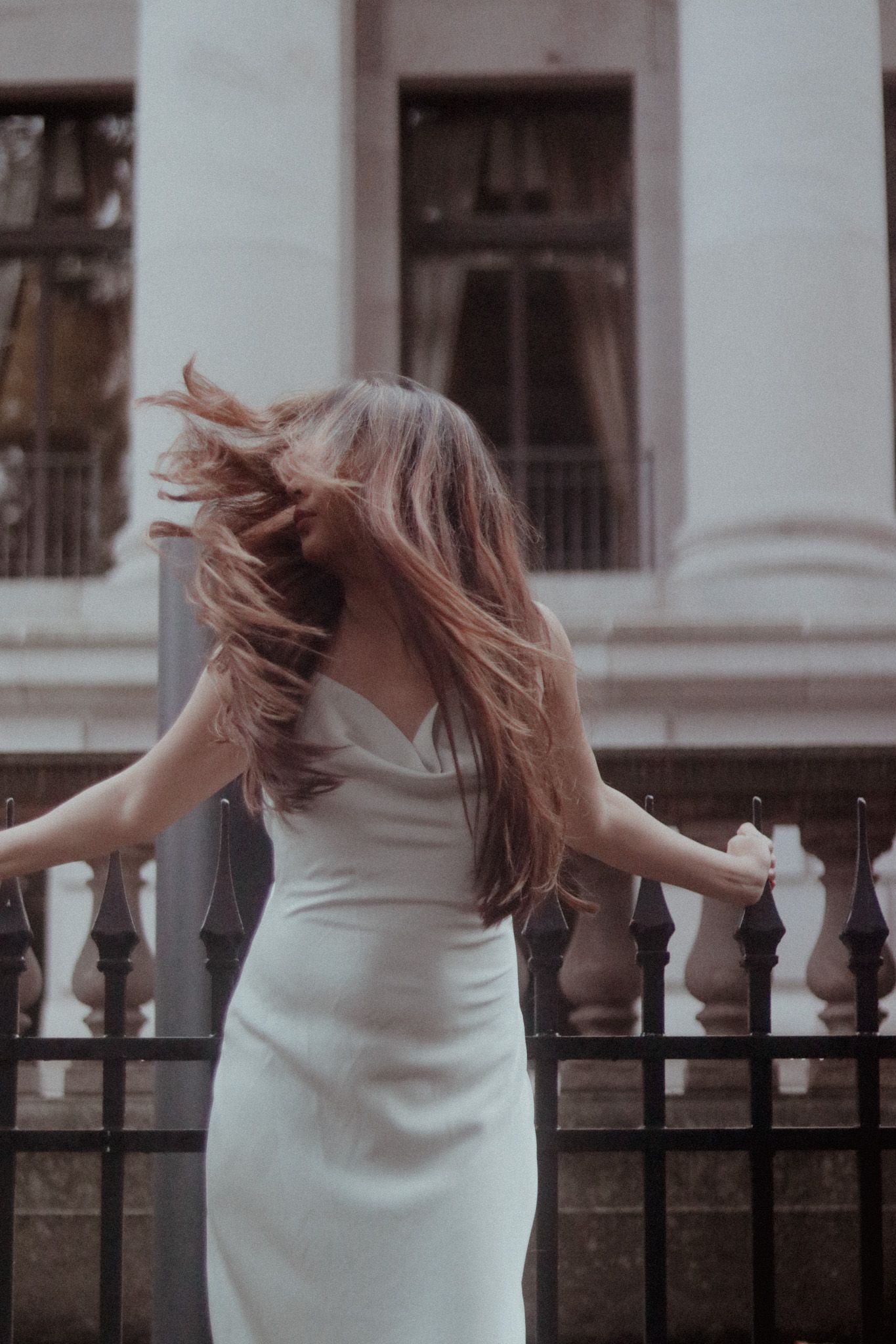 Romantic portrait of a woman in white dress twirling by an ornate balcony railing.