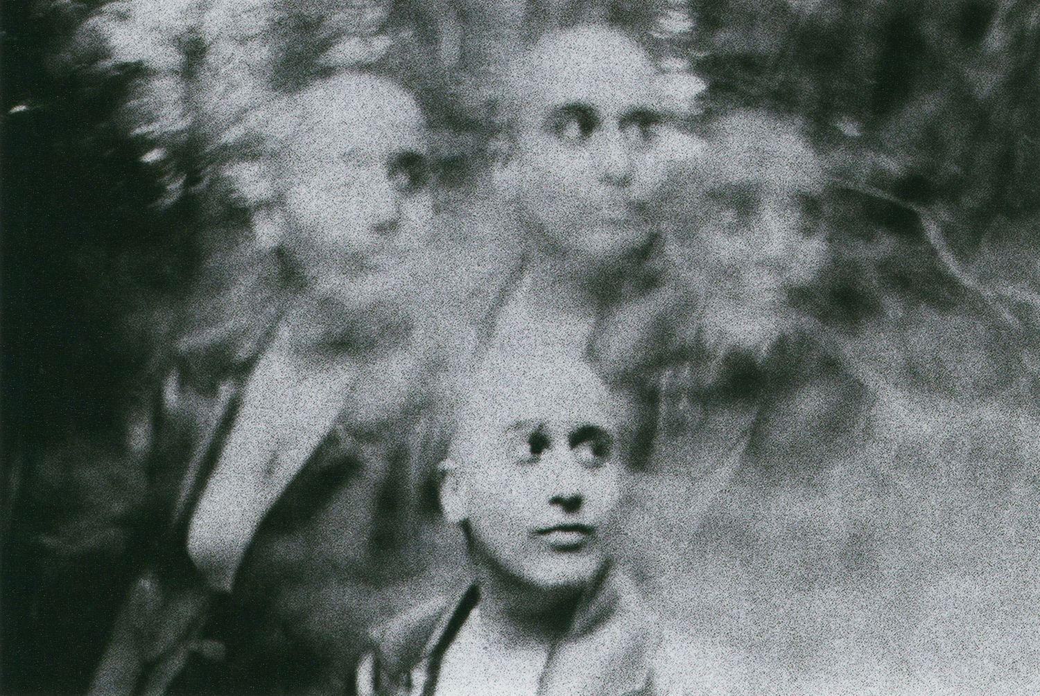 An eerie black and white vintage group photo with blurred ethereal faces creating a ghostly atmospheric effect.