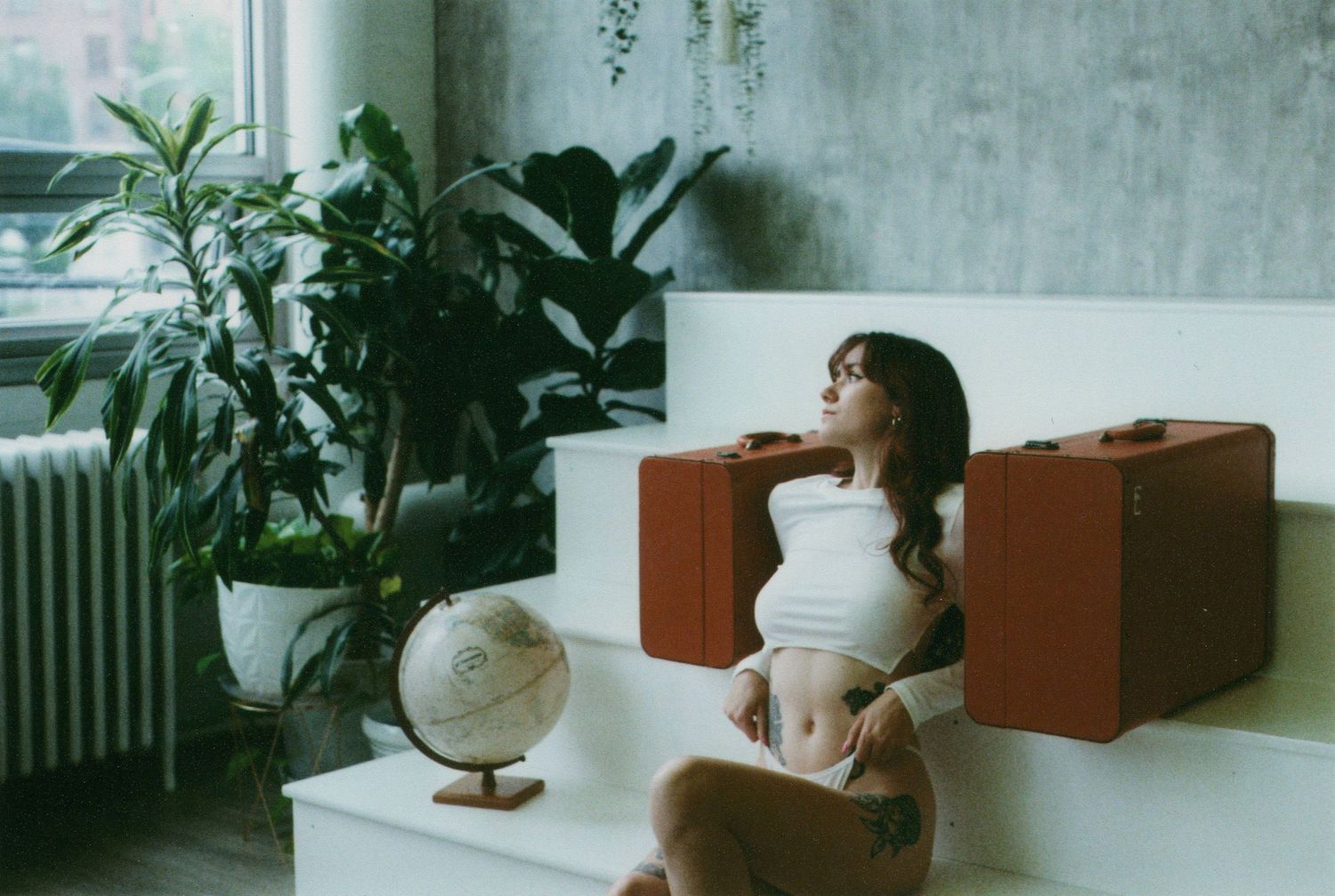 A vintage-style interior scene with brown suitcases, a globe, and potted plants near a window.