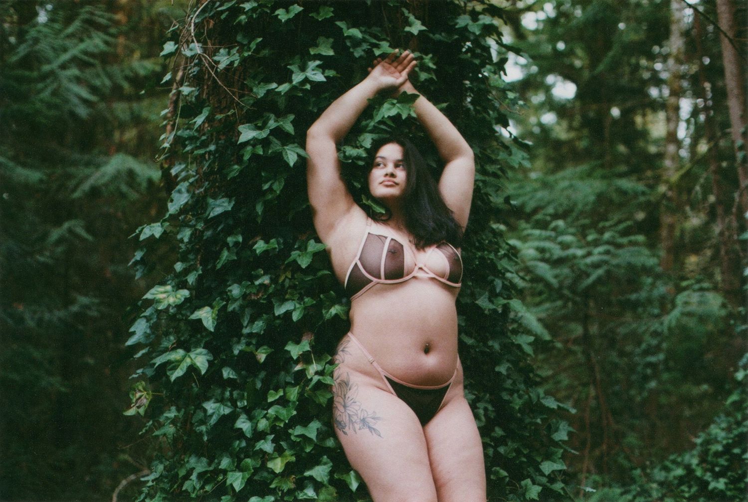Body positive portrait of a woman in lingerie posing confidently in a forest setting.