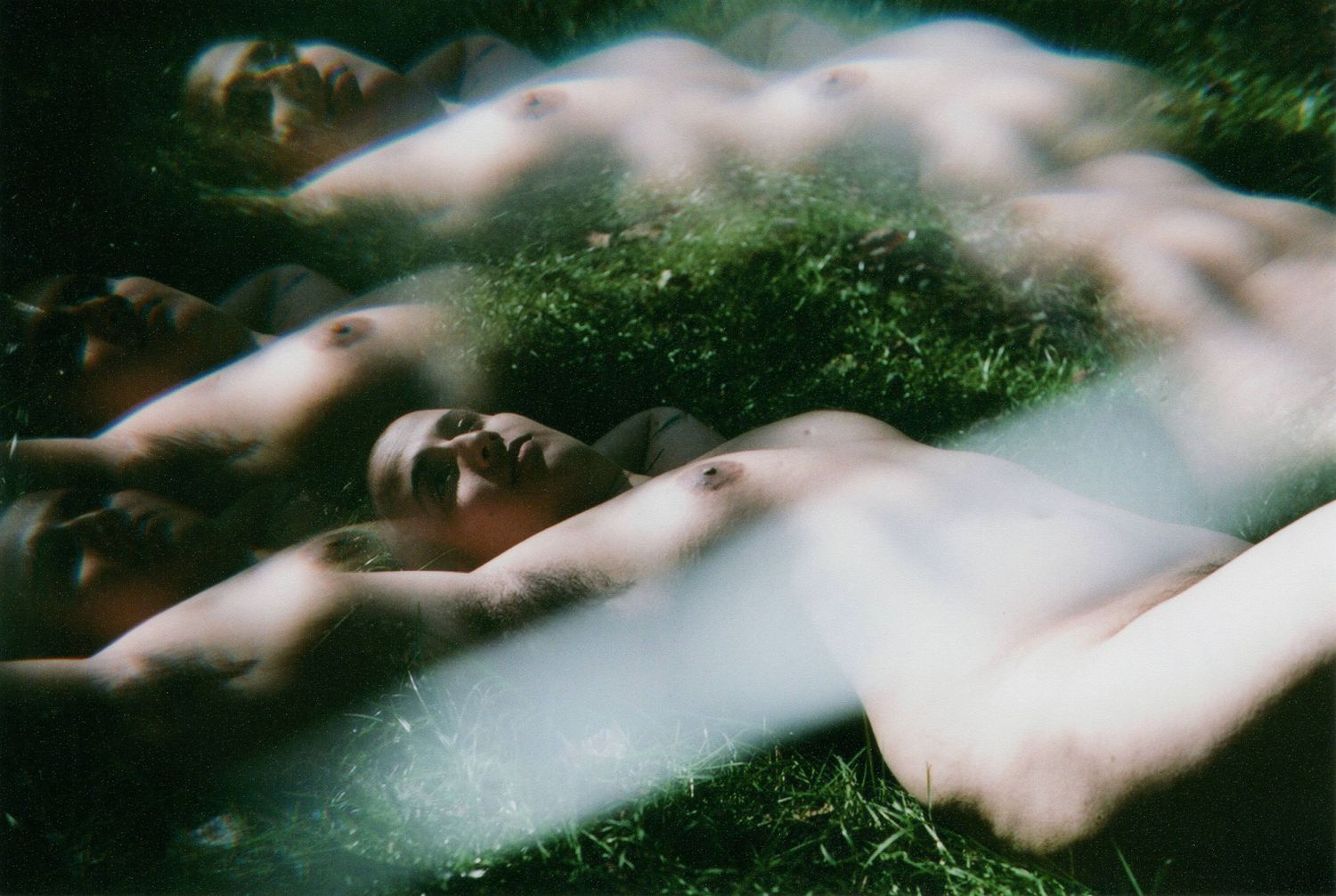 Ethereal multiple exposure photograph of figures laying in grass with misty overlay.
