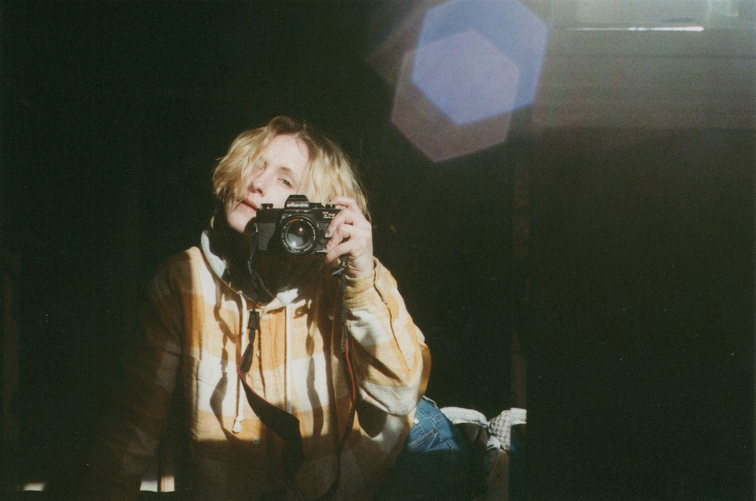 Photographer with camera wearing light colored clothing in dark setting with lens flare.