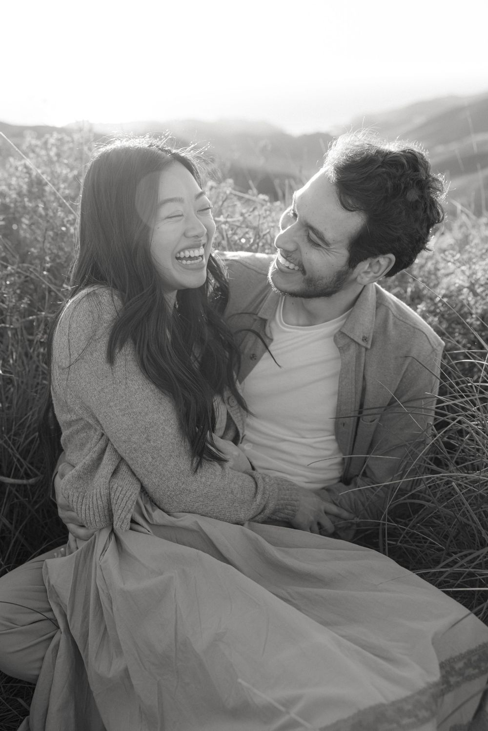 Black and white portrait of a couple sharing a joyful moment together outdoors in a field.