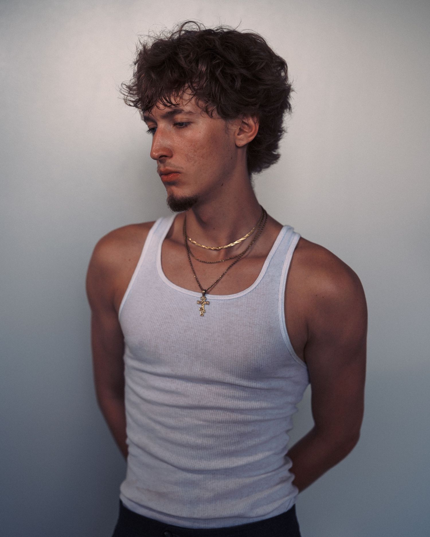 Four similar photos showing a person in a white tank top posing against a light background with moody lighting.